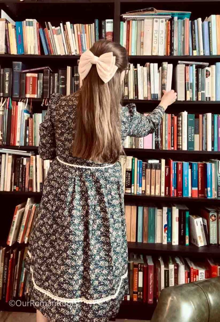 Woman in floral dress choosing books from bookcase.